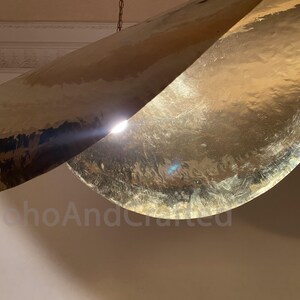 May include: A gold-toned metal pendant light fixture with two curved, overlapping panels. The light fixture is hanging from a chain.