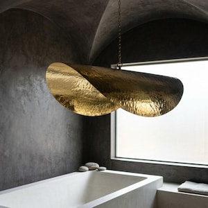 Peut inclure: Une salle de bain moderne avec un grand luminaire suspendu en métal doré martelé. Le luminaire est suspendu au-dessus d'une baignoire blanche, avec une fenêtre en arrière-plan. Les murs sont gris foncé.