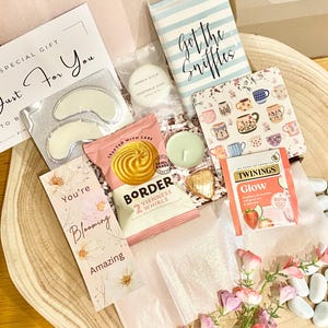 Op de afbeelding: Een geschenkdoos met een Just For You-kaart, oogpatches, Geneva Guild-zeep, een Got the Sniffles-zakdoekjespakket, een onderzetter met mokpatroon, Border Viennese Whirls-koekjes, een waxinelichtje, een hartvormige chocolade en Twinings Glow-thee.