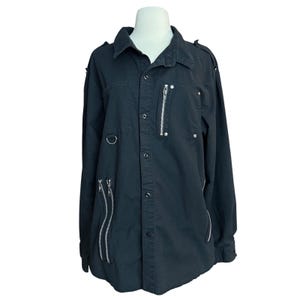 May include: Black button-down shirt with long sleeves, a collar, and multiple silver zippers. The shirt has two chest pockets and a metal ring detail. The fabric appears to be a sturdy cotton or similar material.