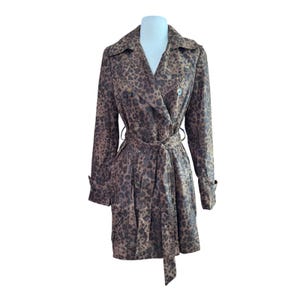 May include: A double-breasted trench coat with a leopard print pattern in shades of brown and black. The coat features a belt, notched lapels, and button details. The coat is displayed on a white mannequin.