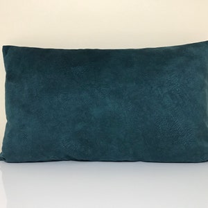 Op de afbeelding: Een rechthoekig, teal-kleurig decoratief kussen met een getextureerd oppervlak. Het kussen is geplaatst op een wit oppervlak en de achtergrond is lichtbeige van kleur. Het kussen is effen van kleur en heeft een zachte, pluche uitstraling.