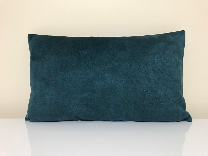 Op de afbeelding: Een rechthoekig, teal-kleurig decoratief kussen met een getextureerd oppervlak. Het kussen is geplaatst op een wit oppervlak en de achtergrond is lichtbeige van kleur. Het kussen is effen van kleur en heeft een zachte, pluche uitstraling.
