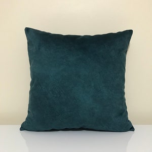 Op de afbeelding: Een vierkant decoratief kussen in teal. Het kussen heeft een getextureerde, su&egrave;de-achtige uitstraling. Het kussen ligt op een wit oppervlak. Een item voor in huis.