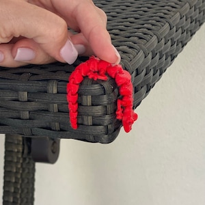 May include: A red 3D printed gecko figurine is perched on the edge of a black wicker table.