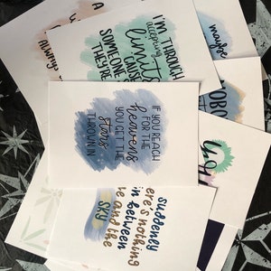 May include: A set of 10 watercolor cards with inspirational quotes. The cards feature a variety of colors, including blue, green, and pink. The quotes are printed in black ink and are centered on the cards. The cards are perfect for adding a touch of inspiration to your home or office.