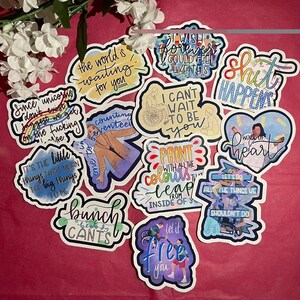 May include: A collection of colorful stickers with various inspirational quotes and phrases. The stickers feature a variety of designs, including hearts, stars, and abstract patterns. Some of the quotes include "The world is waiting for you", "Let it free you", "Work of heart", and "It's the little things that mean the big things to me".