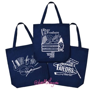 May include: Three navy blue tote bags with white graphic designs. One bag features musical instruments, another displays a produce crate with text, and the third has tailor-related imagery and text. The bags have long handles.