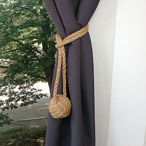 May include: A dark gray curtain with a brown rope tieback. The rope is tied in a knot at the bottom, creating a decorative tassel.