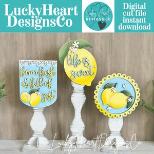 May include: Three wooden lemon-themed decorations on white pedestals. One sign reads "farm fresh & full of zest", another features a lemon with "life is sweet", and the third has lemons. The decorations are in yellow, blue, and white.