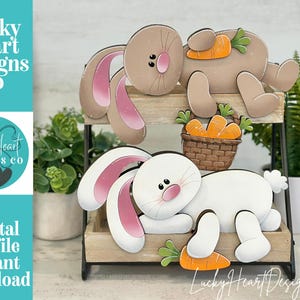May include: Wooden bunny decorations in brown and white, with pink inner ears and carrot accents. One bunny is brown, the other white. A small basket of carrots is also included. The text "Lucky Heart Designs Co" and "Digital cut file instant download" are visible.