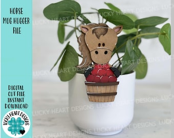 May include: A brown horse mug hugger with a red apple basket. The horse is holding a basket of red apples. The mug hugger is sitting on a white planter with a green plant.