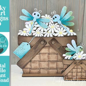 May include: A decorative wooden picnic basket with a woven design, filled with white daisies and topped with blue dragonflies. A smaller basket is also present. The image includes the text "Dragonflies Welcome Spring".