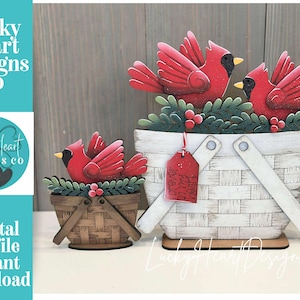 May include: Wooden cardinal bird decorations in a basket. The cardinals are red with black accents and sit atop green foliage with red berries. The basket is white with a woven design and a red tag that says "forever in my heart."