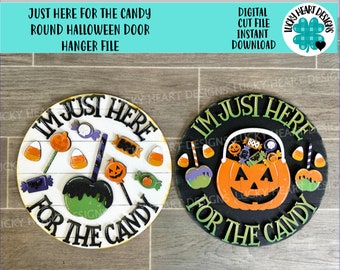 Puede incluir: Dos colgadores de puerta redondos para Halloween, uno negro y uno blanco, con el texto "I'm Just Here For The Candy" en una fuente verde y negra. El colgador negro presenta una calabaza con un cubo de dulces y maíz dulce. El colgador blanco presenta una manzana verde con maíz dulce y una piruleta.