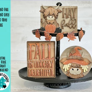 May include: A three-tiered tray decorated with fall-themed wooden signs and figurines. The top tier features a sign that says "Hay Fall" and a Highland cow figurine holding a pumpkin. The middle tier features a sign that says "Fall is Udderly Delightful". The bottom tier features a round wooden sign with a Highland cow wearing a witch's hat.