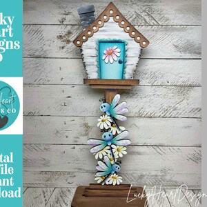 May include: A wooden birdhouse with a light blue door and a daisy. Below the birdhouse are three dragonflies and daisies. The text "Lucky Heart Designs Co" and "Digital cut file instant download" are visible.
