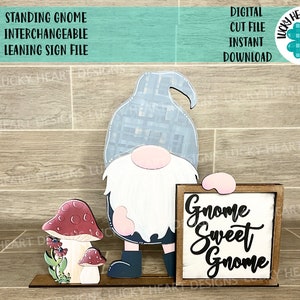 Może przedstawiać: Stojący gnom z szarym kapeluszem i białą brodą trzymający drewniany znak z napisem "Gnome Sweet Gnome". Gnom stoi na drewnianej podstawie z dwoma grzybami.