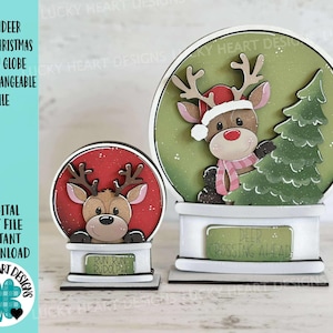 Può includere: Due palle di neve natalizie in legno con disegni di renne. Una ha uno sfondo rosso con il testo "Run Run Rudolph". L'altra ha uno sfondo verde, un albero di Natale e il testo "Deer Crossing Ahead".