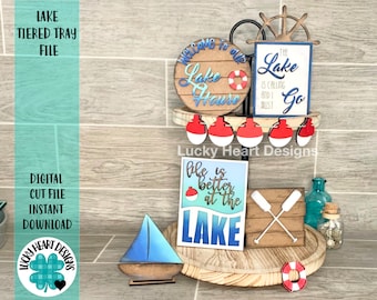 May include: A two-tiered wooden tray with a variety of lake-themed decorations. The top tier features a round wooden sign that says "Welcome to our Lake House" with a life preserver, a wooden sign that says "The Lake is Calling and I Must Go", and a wooden ship's wheel. The bottom tier features a wooden sign that says "Life is Better at the Lake" with a fishing bobber, a wooden sign with two crossed oars, and a small sailboat.