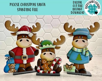 May include: Three wooden moose figurines with Christmas themes. One moose wears a Santa suit, another a green hat and holds a gingerbread man, and the third wears a blue sweater and hat. The text reads "MOOSE CHRISTMAS SANTA STANDING FILE".