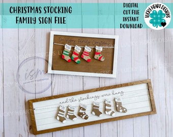 Può includere: Un file di taglio digitale per un cartello natalizio con calze di famiglia. Il cartello presenta uno sfondo bianco con il testo "and the stockings were hung" e una serie di calze con i nomi su di esse. Il cartello è in una cornice marrone.