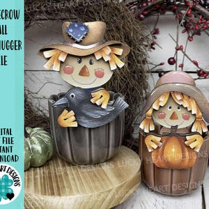 May include: Two wooden scarecrow mug huggers. One features a crow, the other a pumpkin. Both have straw hair, painted faces, and wear hats. The text "SCARECROW FALL MUG HUGGER FILE" is visible.