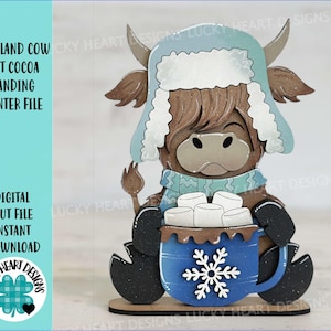 May include: A digital cut file of a Highland cow wearing a blue and white winter hat and scarf, holding a blue mug with a snowflake design and marshmallows. The cow is standing on a wooden base.  The text "HIGHLAND COW HOT COCOA STANDING WINTER FILE" is visible in the image.