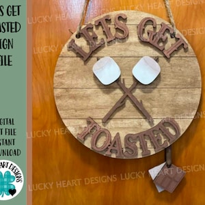 May include: A wooden sign with the text "Lets Get Toasted" in brown lettering. The sign is decorated with two white marshmallows on sticks crossed over each other. The sign is hanging on a brown wooden wall.