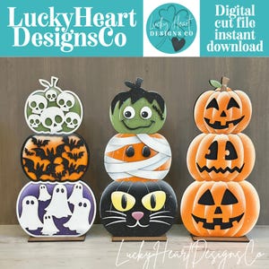 Peut inclure: Trois décorations en bois empilées sur le thème d'Halloween. La pile de gauche présente des crânes, des chauves-souris et des fantômes. La pile centrale montre un monstre de Frankenstein, une momie et un chat noir. La pile de droite est composée de trois citrouilles orange.