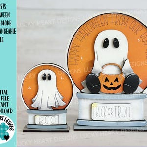 May include: Two wooden Halloween snow globe decorations with ghosts and pumpkins. The larger snow globe has the text "Happy Halloween from our Boo Crew" and the smaller snow globe has the text "Boo".