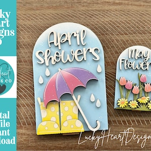May include: Wooden signs with spring themes. One sign says "April Showers" with an umbrella and rain boots. The other says "May Flowers" with tulips and daisies. The signs are light blue with white and pastel accents.