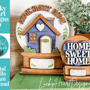 May include: Wooden home decor featuring a blue house with a white heart, the words "Home Sweet Home," and "Our Happy Place." A smaller piece says "Welcome." The design includes green accents and is a digital cut file.