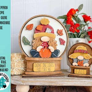 May include: Wooden fall-themed gnome snow globe with a pumpkin, leaves, and the text "Gnome One Loves Fall Like Me." A smaller gnome figure with the word "Fall" is also displayed. The design is perfect for autumn decor.
