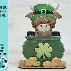 May include: A brown Highland cow wearing a green leprechaun hat peeks out of a green pot of gold. The pot is decorated with a shamrock and surrounded by gold coins.