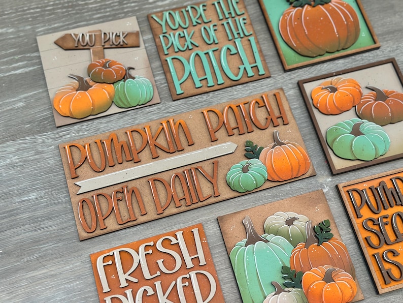 Peut inclure: Ensemble de panneaux en bois avec des motifs de citrouilles et du texte. Les panneaux pr&eacute;sentent des citrouilles orange et vertes, avec des phrases comme "You Pick", "Pumpkin Patch" et "Fresh Picked". Les panneaux sont sur un fond en bois clair.