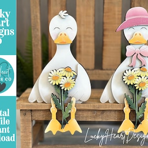 May include: Wooden duck figurines, one with a pink hat and bow, the other without. Both hold bouquets of daisies. The ducks are white with yellow beaks and feet. The text "Lucky Heart Designs Co" and "Digital cut file instant download" are visible.