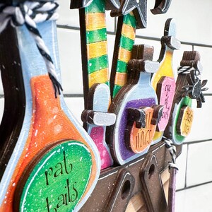 May include: Wooden Halloween decoration featuring witch legs, hats, and potion bottles. The bottles are labelled with names such as "rat tails" and "witch wings".