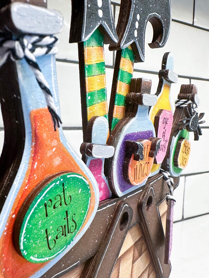 May include: Wooden Halloween decoration featuring witch legs, hats, and potion bottles. The bottles are labelled with names such as "rat tails" and "witch wings".