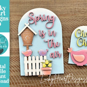 以下が含まれることがあります： 明るい青色の背景に、春をテーマにした木製の装飾。1つは「Spring is in the air」と書かれており、鳥小屋、鳥、花が描かれています。もう1つは「Chirp Chirp」と書かれており、鳥が描かれています。