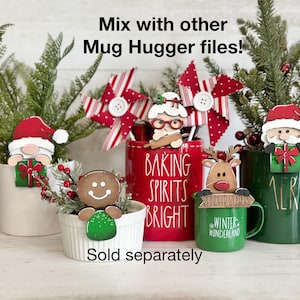 May include: A set of five Christmas-themed mug huggers, including a gingerbread man, a reindeer, a Santa Claus, a woman with a rolling pin, and a snowman. The mug huggers are made of wood and painted in festive colors. The text "Baking Spirits Bright" is printed on a red mug. The text "Winter Wonderland" is printed on a green mug. The text "Reindeer Stables" is printed on a green mug. The text "Merry" is printed on a green mug. The text "Sold separately" is printed below the mugs.