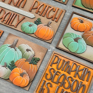 Peut inclure: Panneaux et carr&eacute;s d&eacute;coratifs en bois sur le th&egrave;me de l'automne, avec des citrouilles orange, vertes et cr&egrave;me. Certains panneaux portent des inscriptions telles que "Pumpkin Patch Daily" et "Pumpkin Season is Here". Les citrouilles sont en 3D avec des tiges et des feuilles d&eacute;taill&eacute;es.