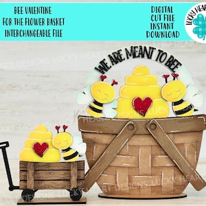 Puede incluir: Un proyecto de artesanía de madera con un diseño de San Valentín con temática de abejas. El diseño incluye una colmena, dos abejas y un corazón. El texto "We are meant to bee" está escrito en un letrero de madera curvo. El diseño está pensado para ser utilizado con una cesta de flores.