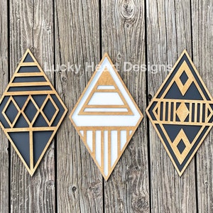 May include: Three geometric wooden wall decor pieces in the shape of diamonds. The diamonds are black and white with a geometric pattern. The diamonds are arranged in a row on a wooden background.