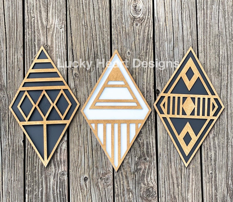 May include: Three geometric wooden wall decor pieces in the shape of diamonds. The diamonds are black and white with a geometric pattern. The diamonds are arranged in a row on a wooden background.
