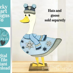 Könnte beinhalten: Eine Holzgansfigur mit blauem Wintermantel, Hut und Schal, verziert mit Schneeflocken. Die Gans hat einen gelben Schnabel und Füße. Der Text auf dem Bild lautet "Hats and goose sold separately."