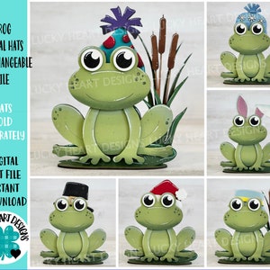 Puede incluir: Conjunto de seis sombreros de rana intercambiables para una figura de rana de madera. Los sombreros incluyen un sombrero de cumpleaños, un sombrero de invierno, un sombrero de orejas de conejo, un sombrero de peregrino, un sombrero de Papá Noel y un sombrero de marinero. La rana está sentada sobre una base verde con juncos.