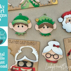 Puede incluir: Adornos navideños de madera con Papá Noel, Mamá Noel y elfos. Los adornos están pintados con colores brillantes y tienen un diseño festivo. El texto "Lucky Heart Designs Co" es visible.