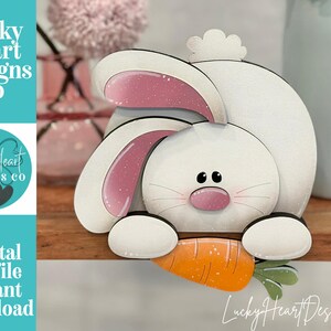May include: A white wooden bunny decoration with pink-lined ears and a pink nose, holding an orange carrot. The design includes the text "Lucky Heart Designs Co" and "Digital cut file instant download".