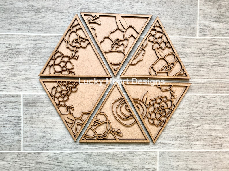 May include: Six wooden triangular coasters with intricate floral designs cut out. The coasters are arranged in a hexagonal pattern. The text "Lucky Heart Designs" is visible in the center.